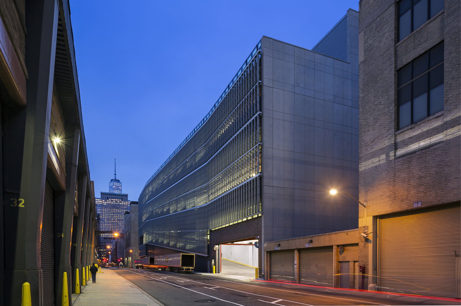 View of DSNY garage along a narrow street with One World Trade Center in the background.