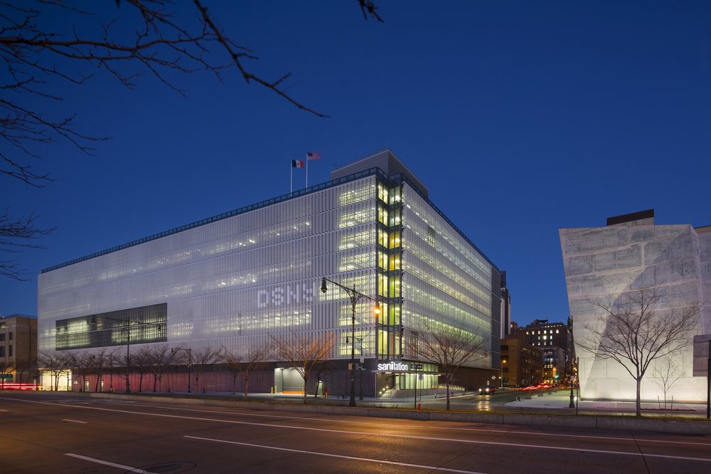 Evening view of a modern glass-clad building with "sanitation" signage visible.