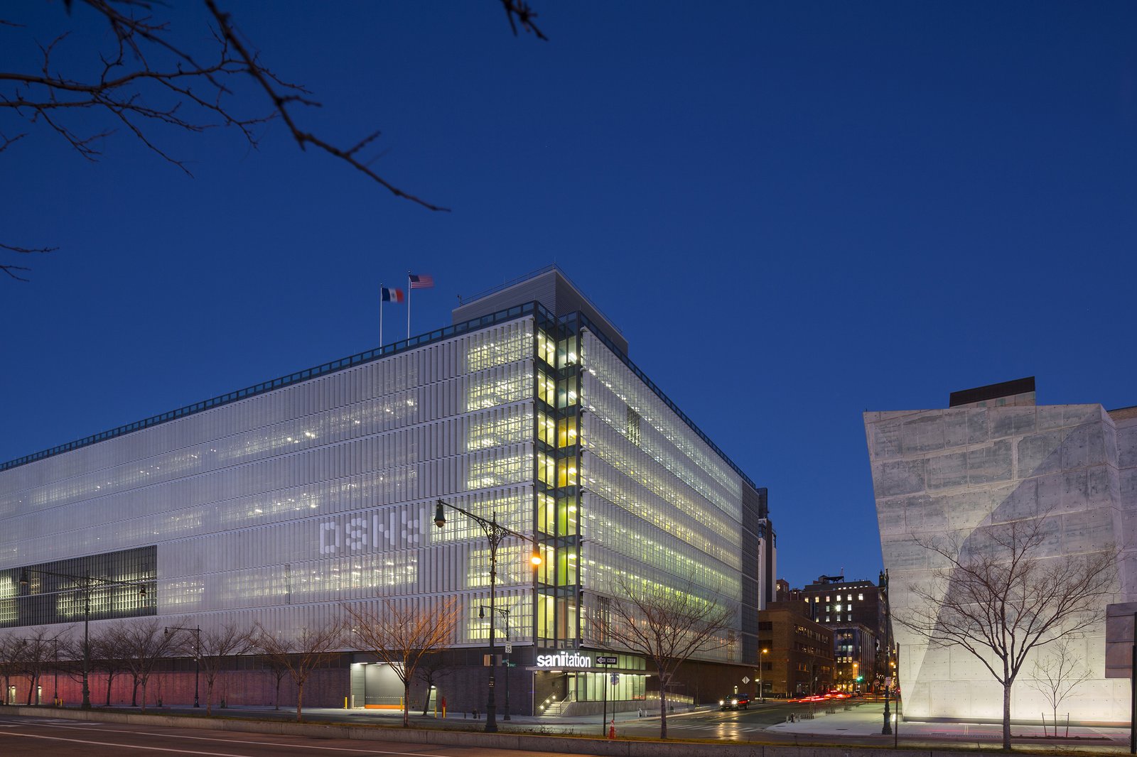 Evening view of a modern glass-clad building with "sanitation" signage visible.