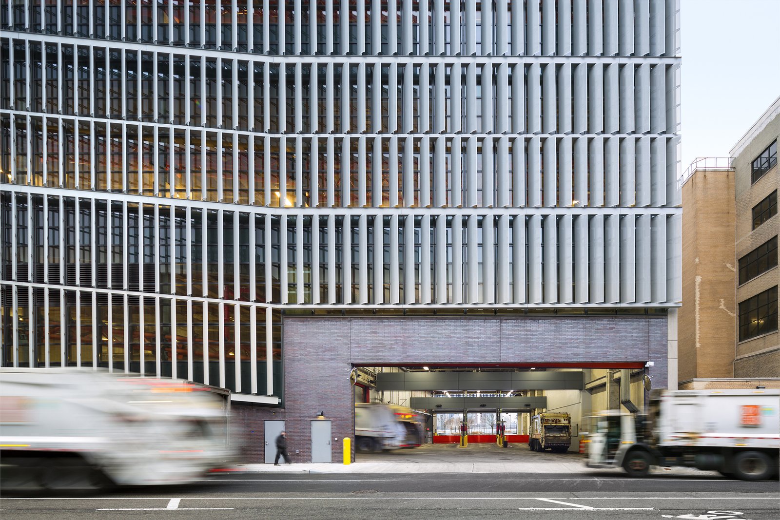 Street view of DSNY garage entrance with sanitation trucks moving in and out.