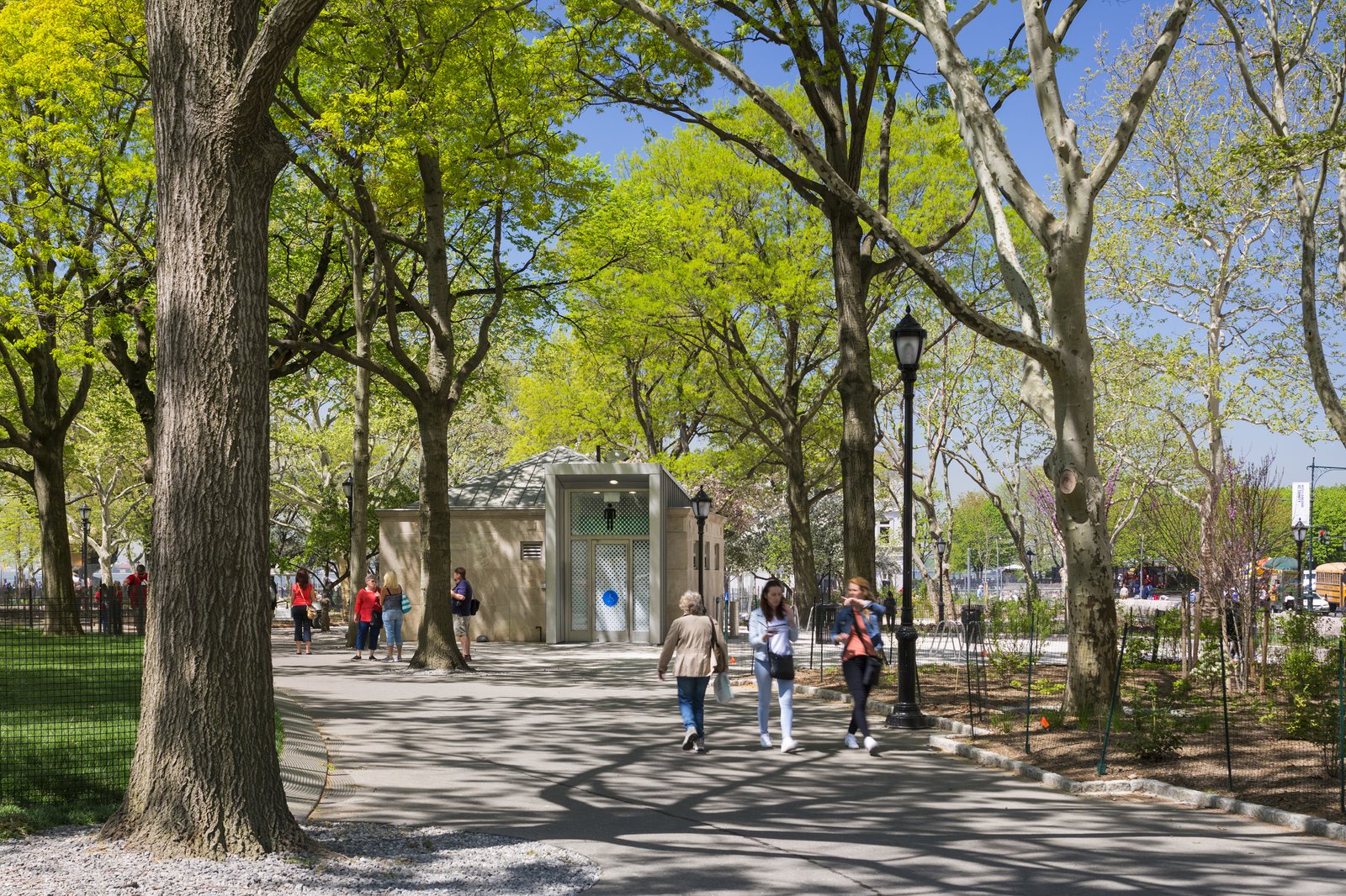 Comfort station surrounded by trees and pathways, with people walking nearby in Battery Park.