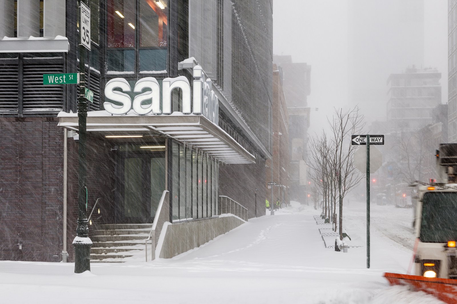 An exterior view of DSNY garage entrance with snow-covered streets and sanitation truck.