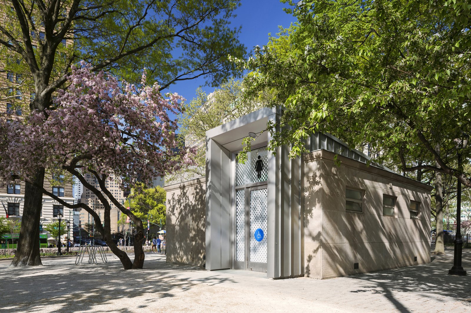 A modernized comfort station with a restored limestone façade surrounded by trees in Battery Park.