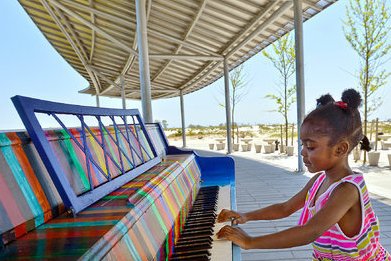 A young girl plays a colorful outdoor piano under a metal canopy in a park.