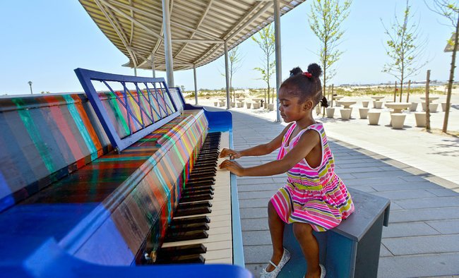 A young girl plays a colorful outdoor piano under a metal canopy in a park.