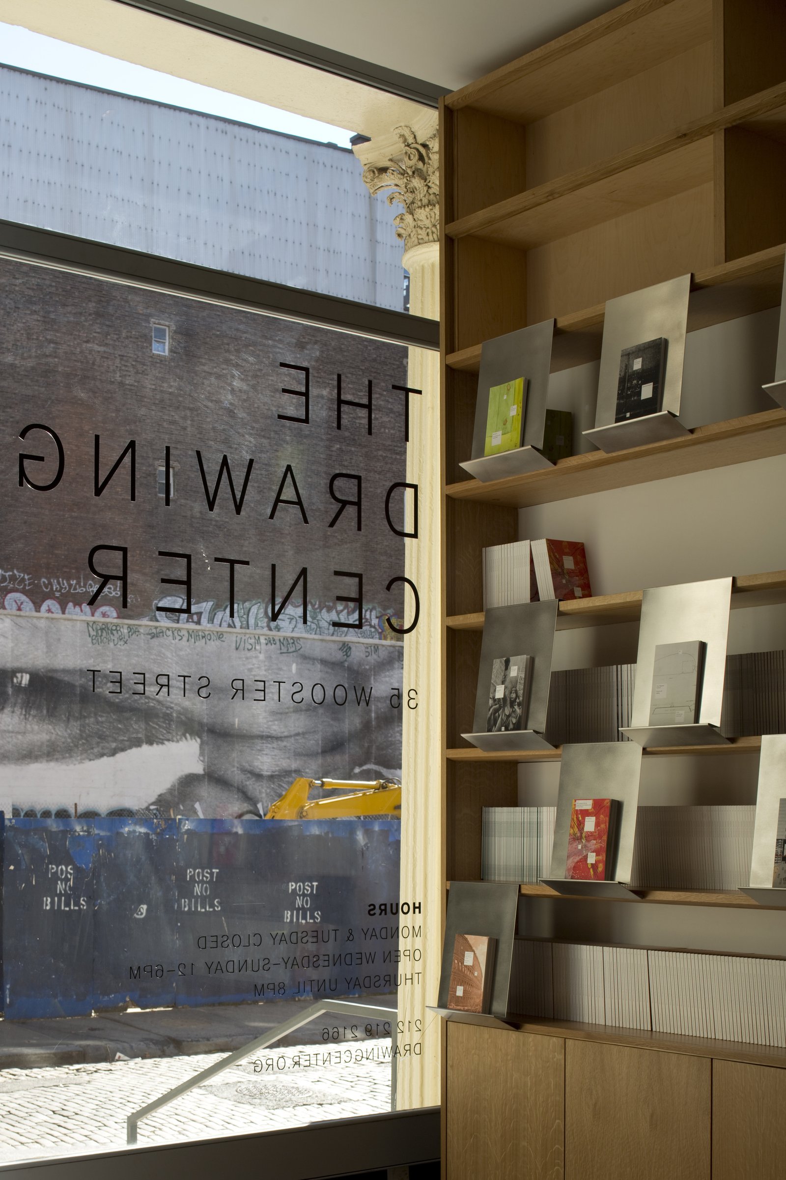 Display shelves with books beside a window with The Drawing Center signage.