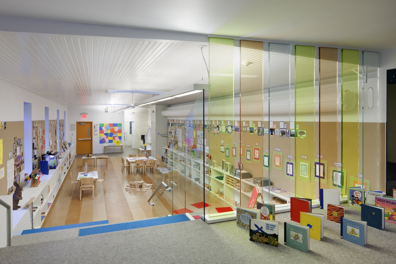 View of a nursery school classroom with colorful glass partitions, books, and child-sized furniture.