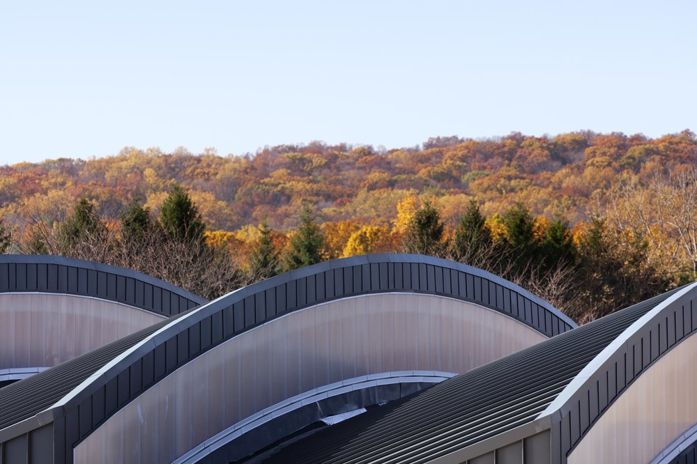 Curved metal roofs with translucent panels contrast against a backdrop of autumn foliage.