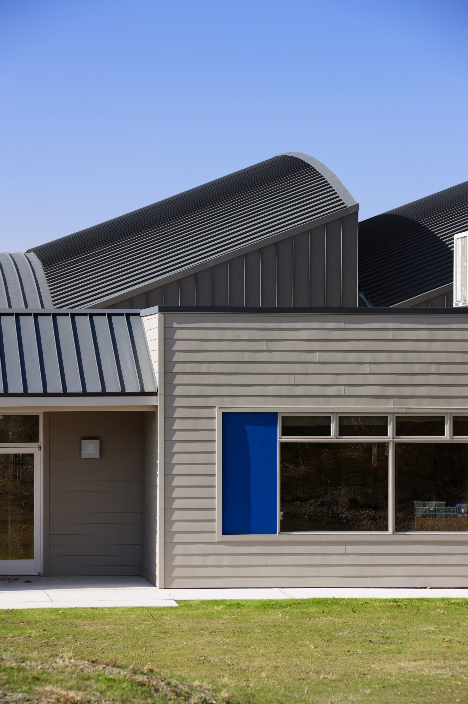 A school building with curved metal roofs, horizontal siding, and a blue accent panel.