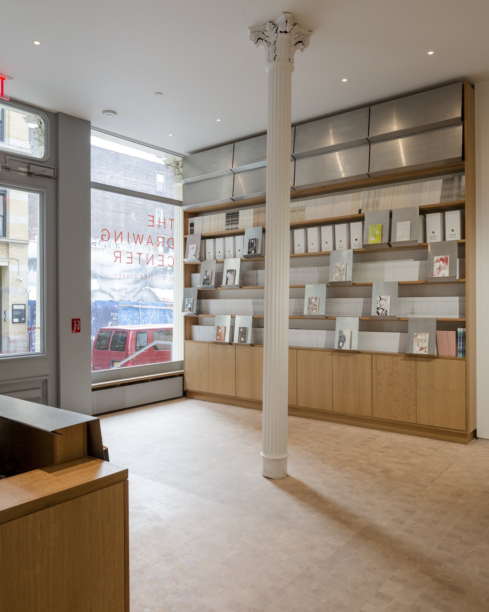 Gallery bookstore space with floor-to-ceiling wooden shelving, original Corinthian column, and large storefront window.