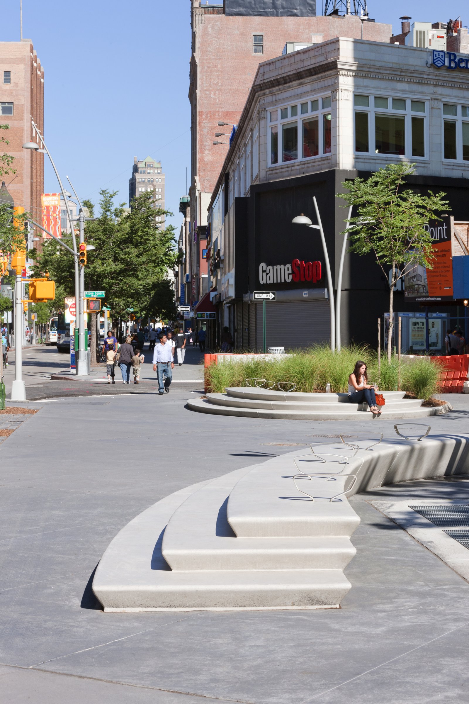 Curved seating with integrated planters in an urban plaza surrounded by retail buildings.