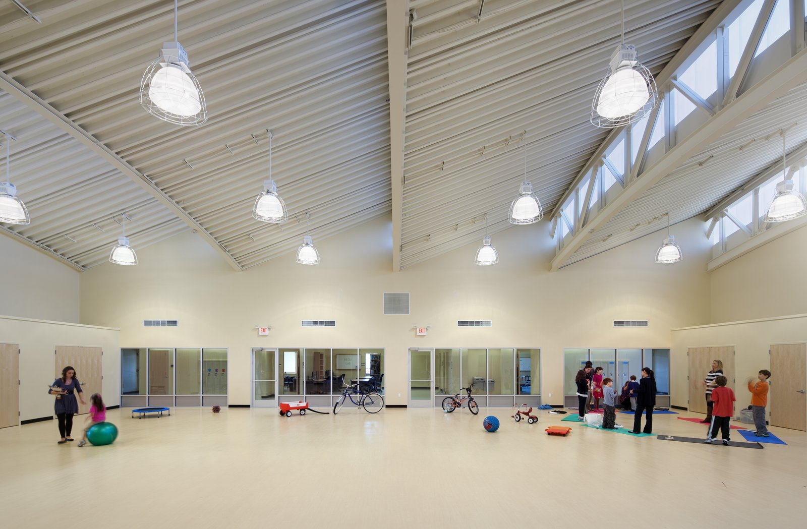 A spacious activity room with high ceilings, exposed trusses, and children engaged in play.