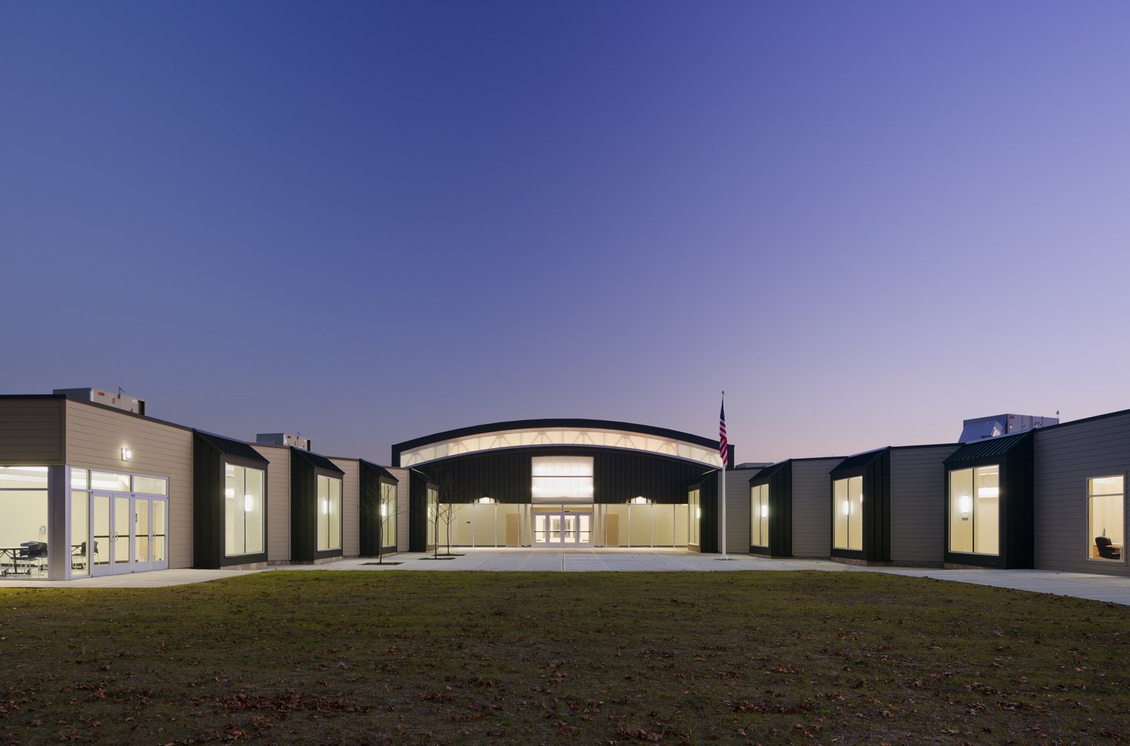 A modern school building with a curved central volume flanked by two wings, illuminated at dusk.