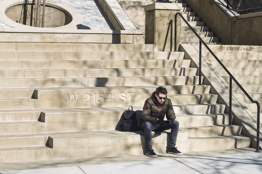 A man sits on engraved concrete steps with handrails and a lamppost; trees and stairs are visible.