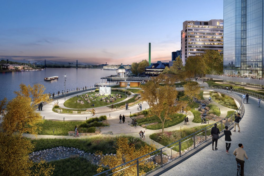 Elevated view of an urban riverfront park with a lawn, paths, and waterfront promenade.