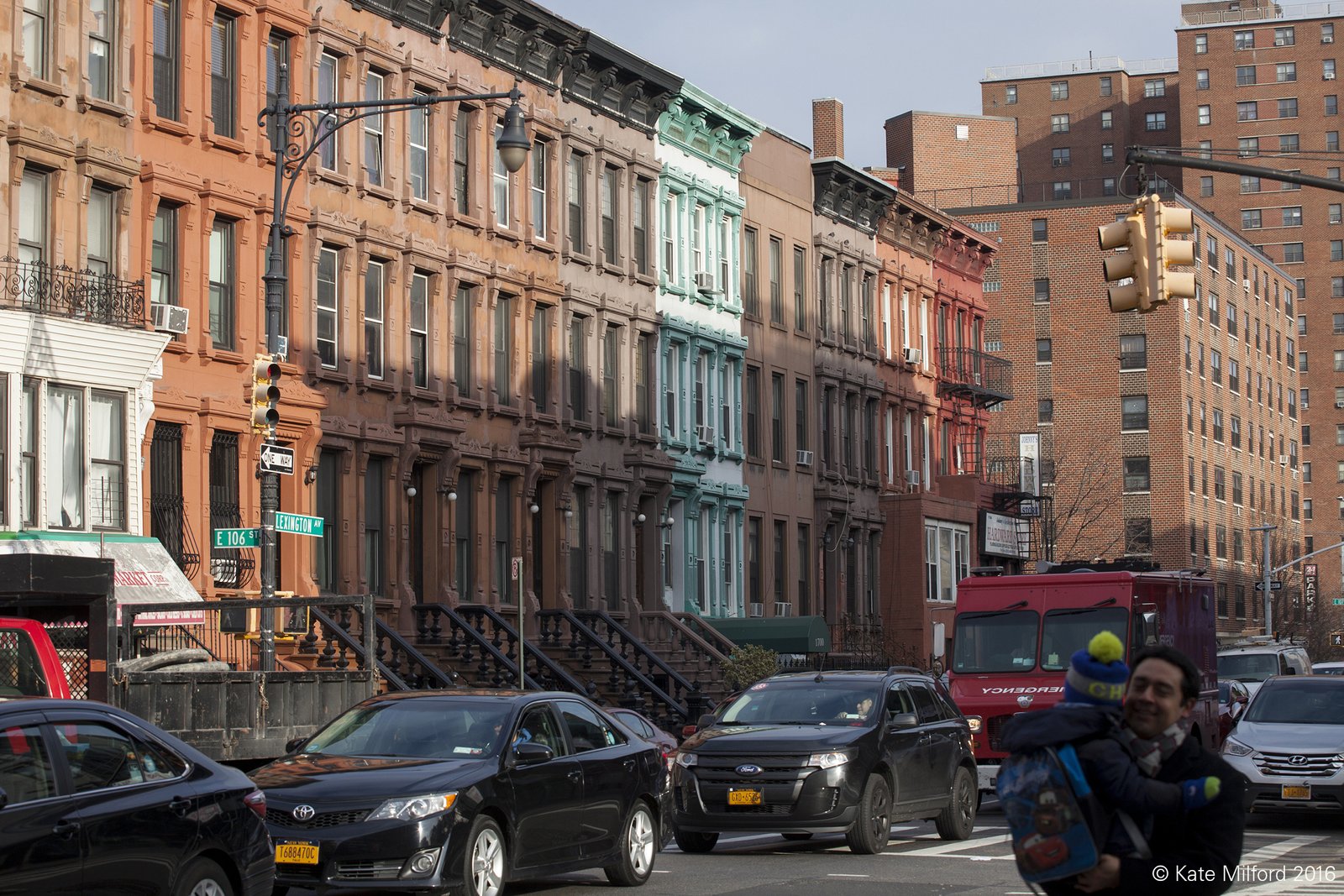 Row of brownstones with cars and people in the street.