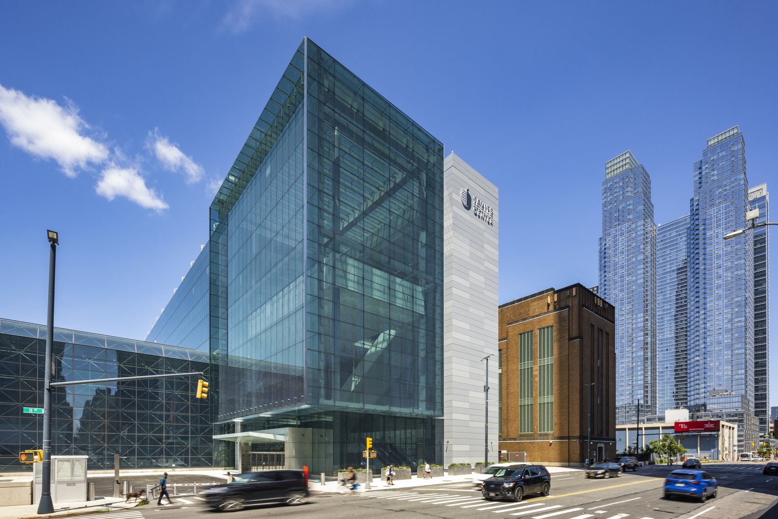 The modern cultural center features a transparent glass curtain wall that contrasts with a historic brick building nearby.