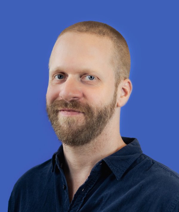 Headshot of Pierre de Brun in a blue shirt against a blue background.