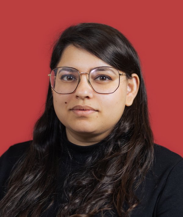 Headshot of Manasi Punde in a dark top against a red background.