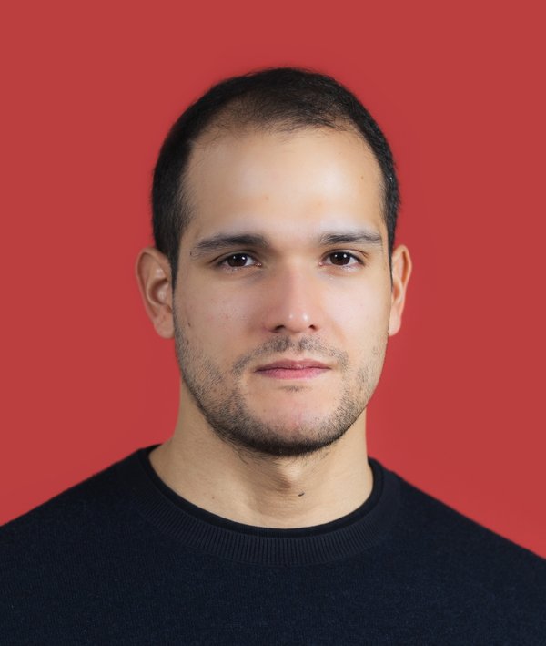 Headshot of Santiago Vasquez Carvajal in a dark shirt against a red backdrop.