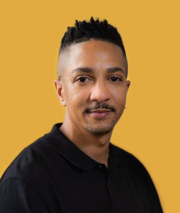 Headshot of Chris Rice with a dark shirt and yellow background.