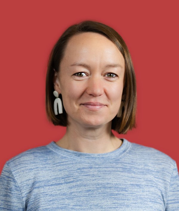 Headshot of Annie Peyton in a grey shirt against a red background.