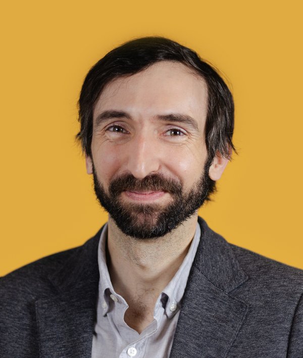 Headshot of Jacob Dugopolski with a grey blazer and yellow background.