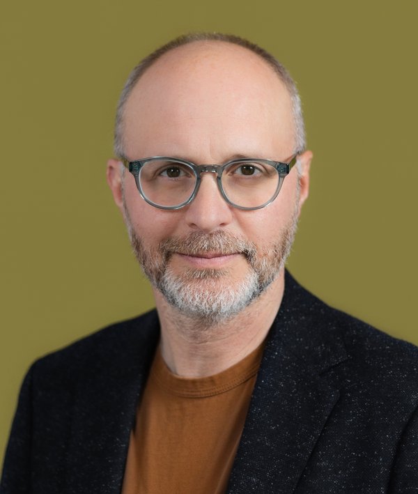 Headshot of Adam Lubinsky with a dark blazer and green background.