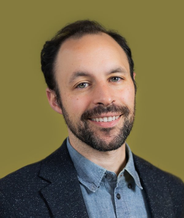 Headshot of David Vega-Barachowitz with a grey blazer and green background.