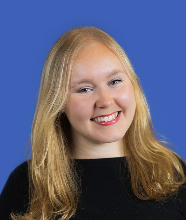 Headshot of Ella Sprick in a black top against a blue background.