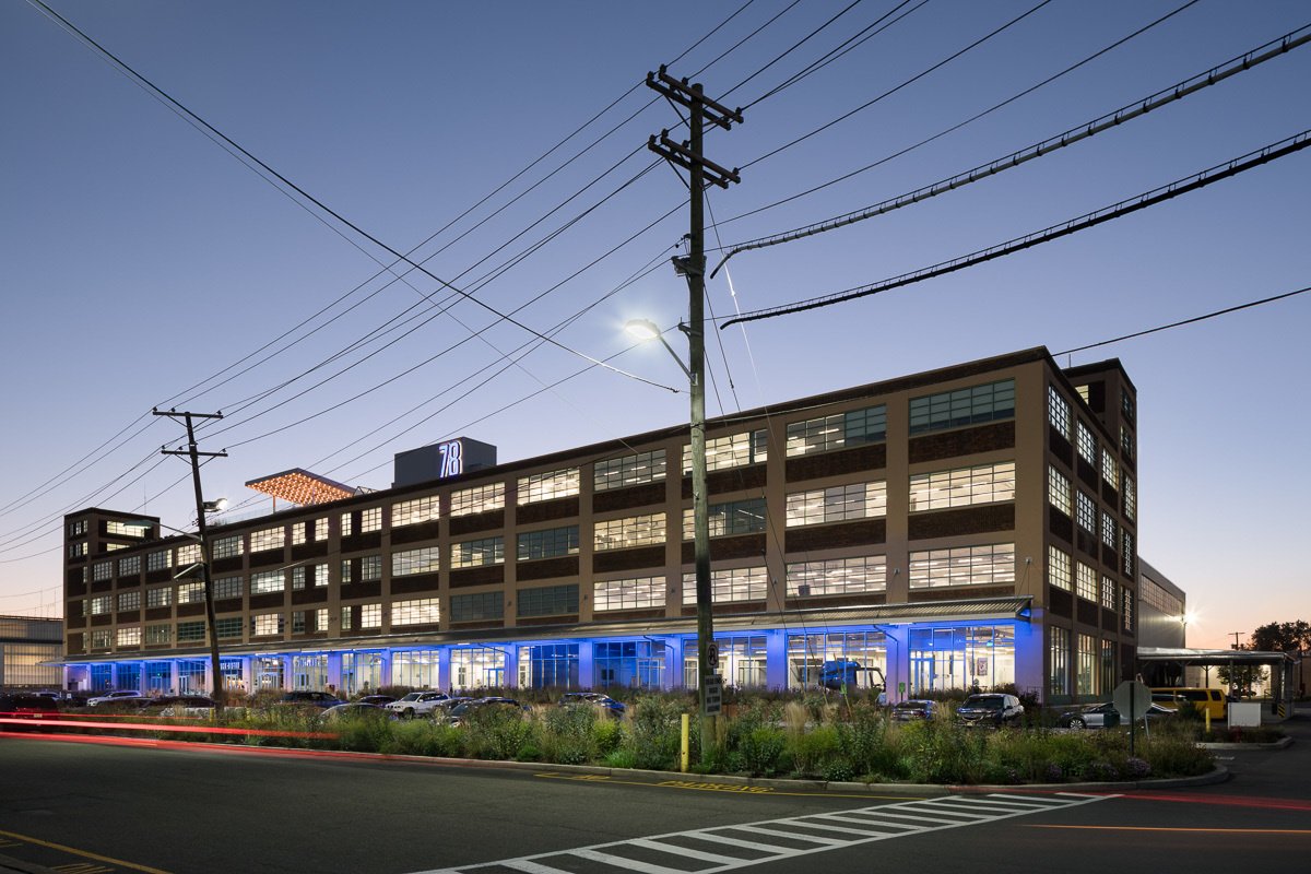 Renovated industrial building at dusk with illuminated blue ground floor retail and gridded windows above.