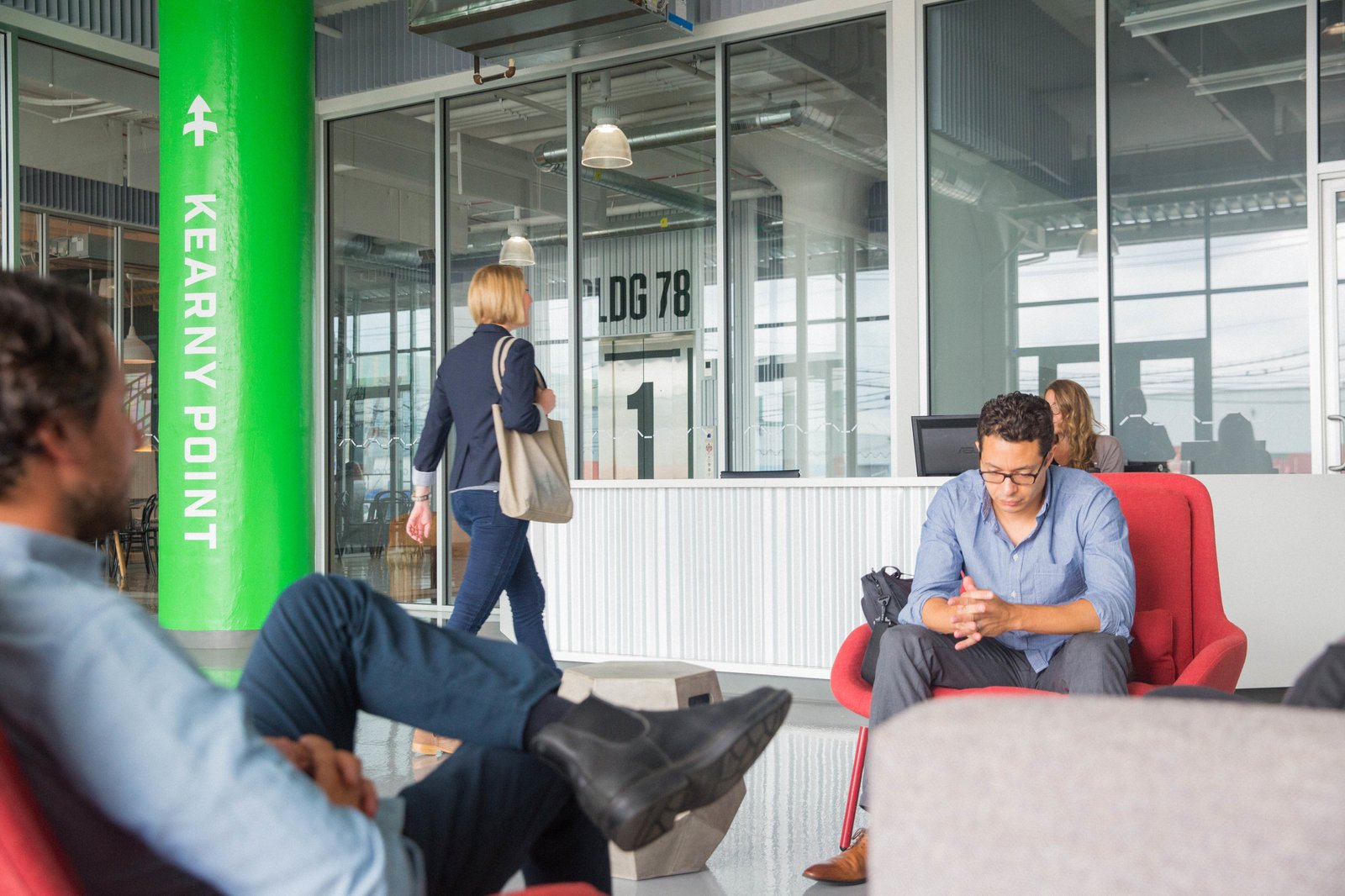 The entrance with bright green Kearny Point wayfinding column, people seated in red chairs near glass doors.