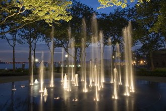 Fountain lights glow beneath tree branches at night in a tranquil park setting.