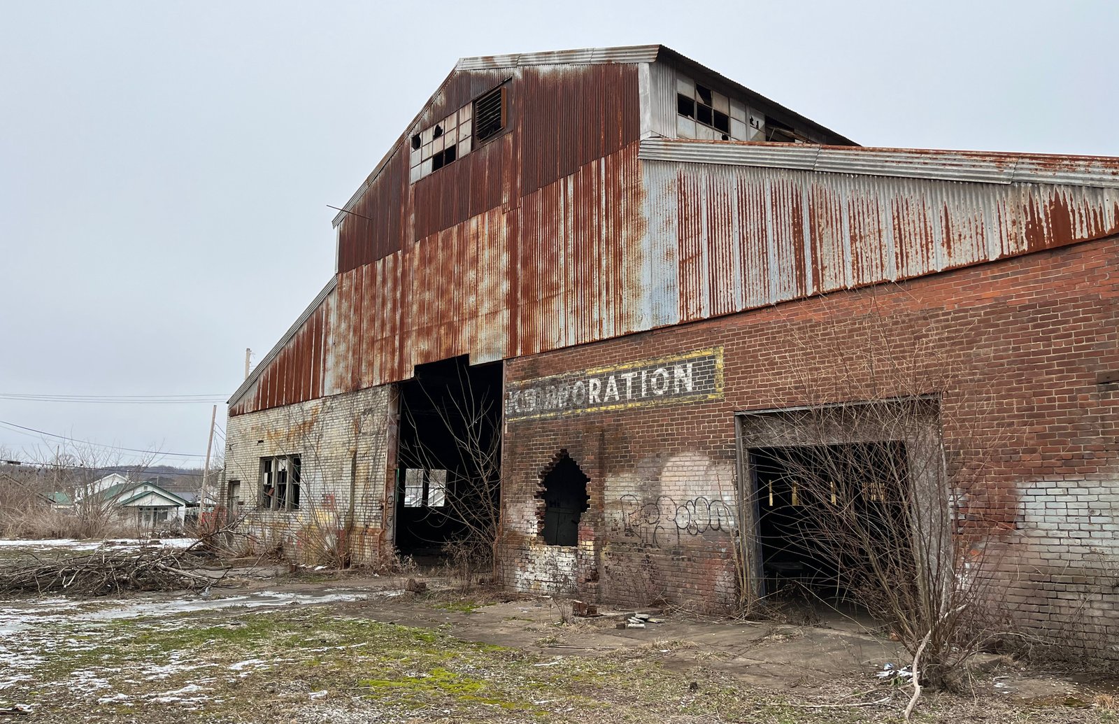 Rusty exterior of an abandoned industrial building with overgrown vegetation.