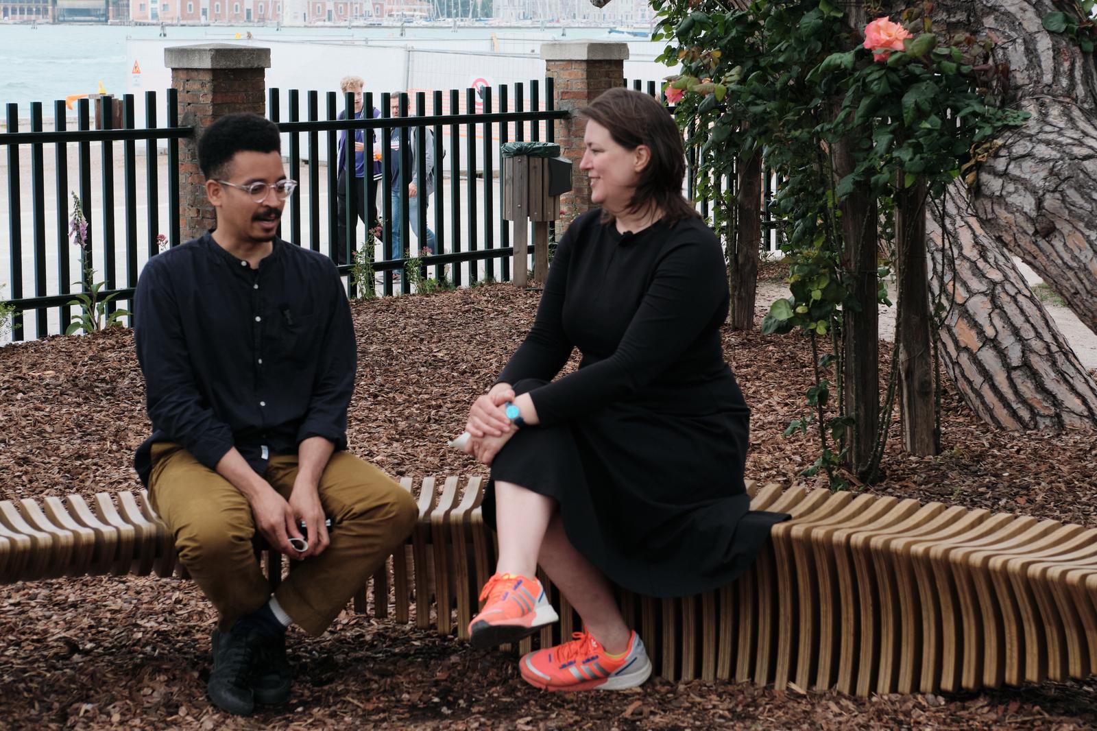 Two people sitting on the curved bench having a conversation.