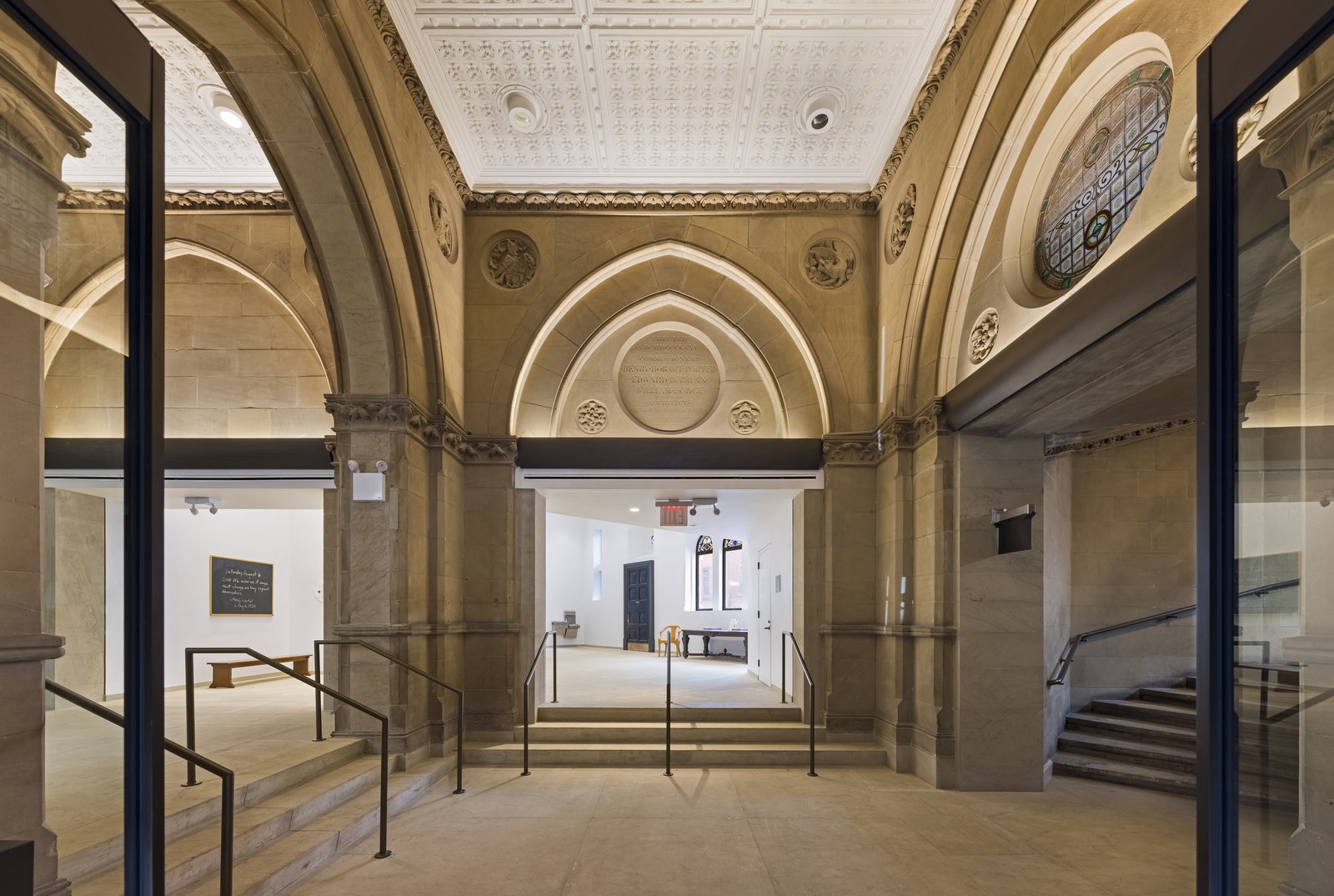 An entrance hall has stone walls and arched ceilings with railings on steps that lead to three doorways.