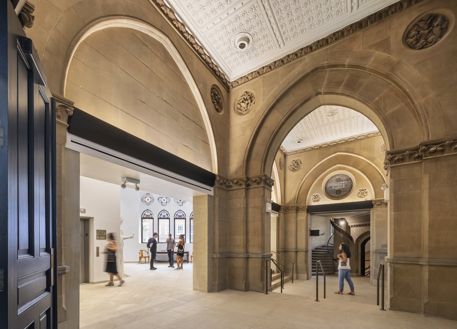 A stone hallway with arched doorways leads to multiple rooms, with handrails on steps and decorative windows ahead.