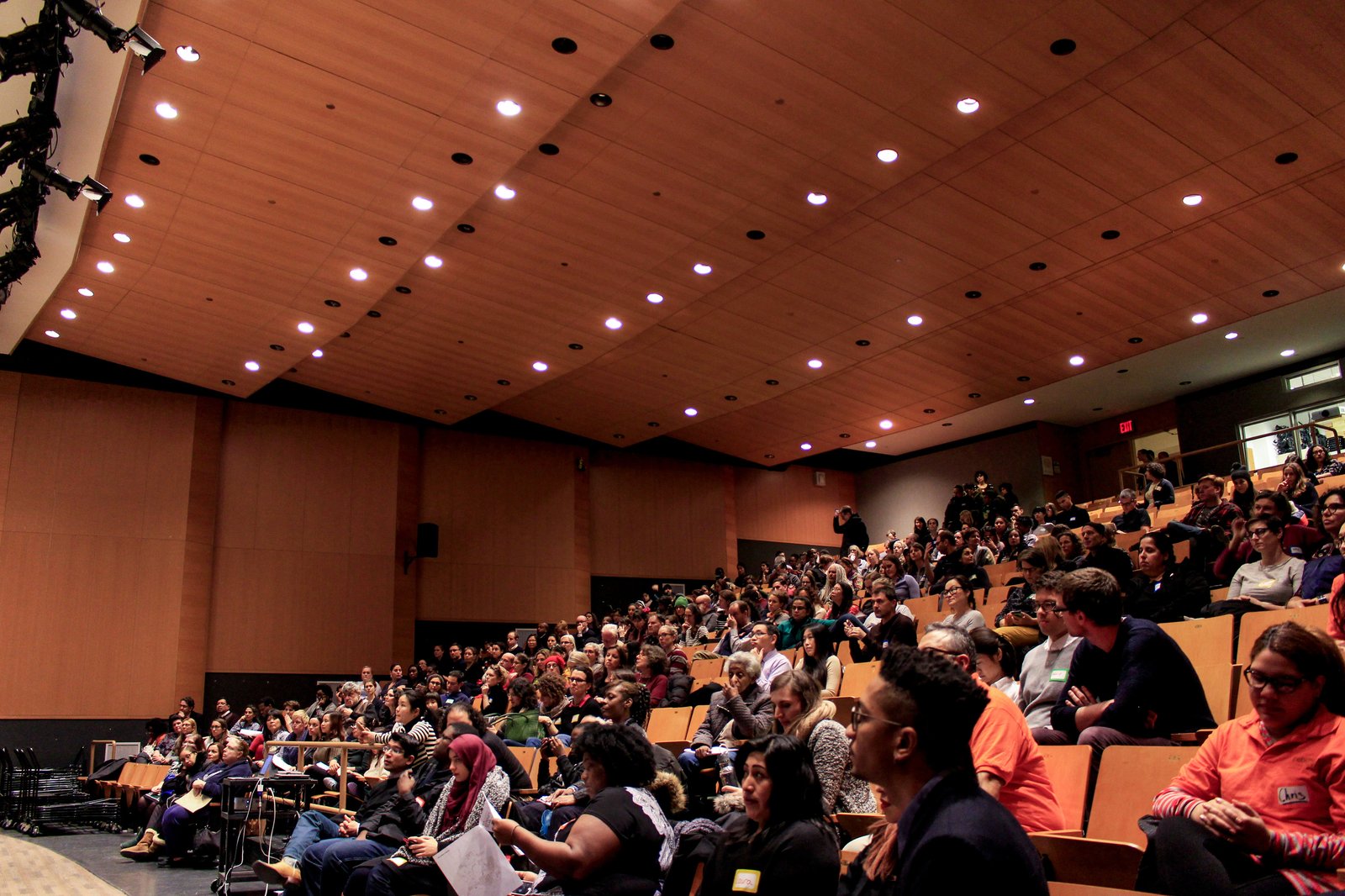 A full audience in an auditorium attentively listens to a speaker.