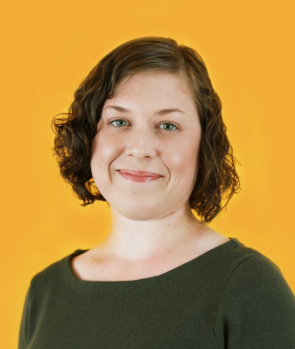 Headshot Kendall Baldwin wearing a green sweater against a yellow background.