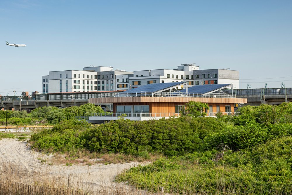 An image of the Coastal Conservation Center with solar panels, set between the beach dunes and nearby urban buildings