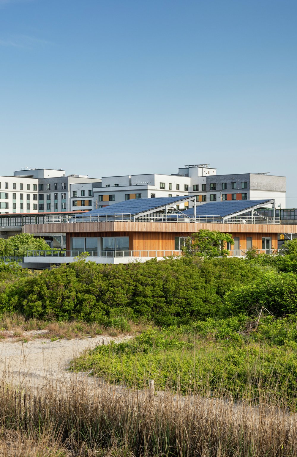 An image of the Coastal Conservation Center with solar panels, set between the beach dunes and nearby urban buildings