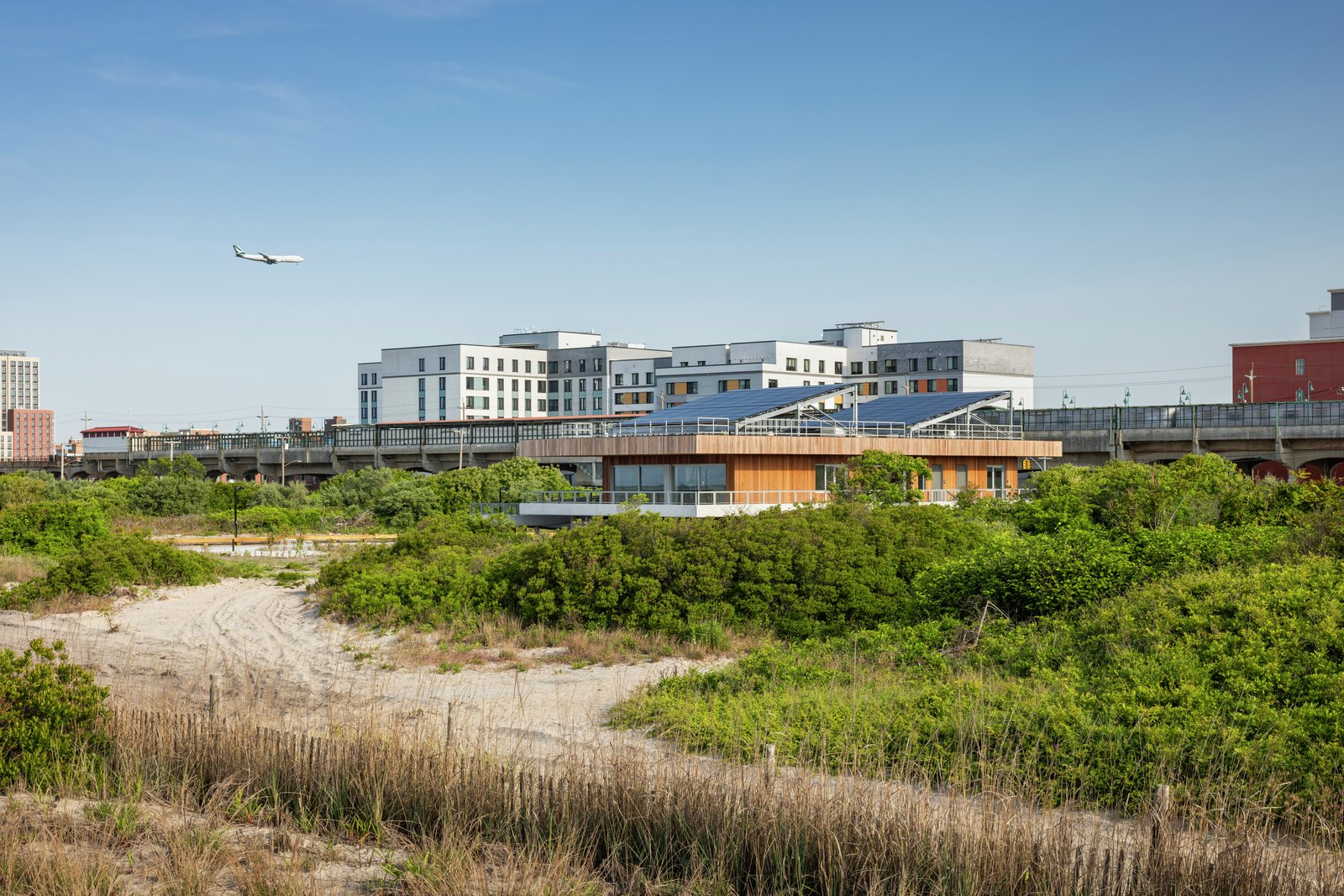 An image of the Coastal Conservation Center with solar panels, set between the beach dunes and nearby urban buildings