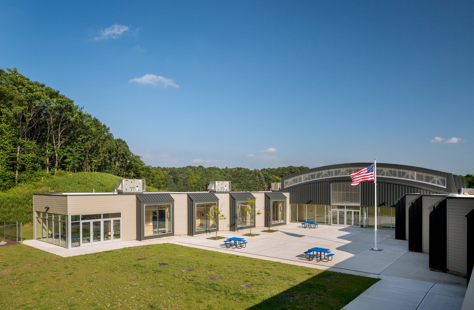 A modern school courtyard with modular wings, a curved central hall, and outdoor seating.