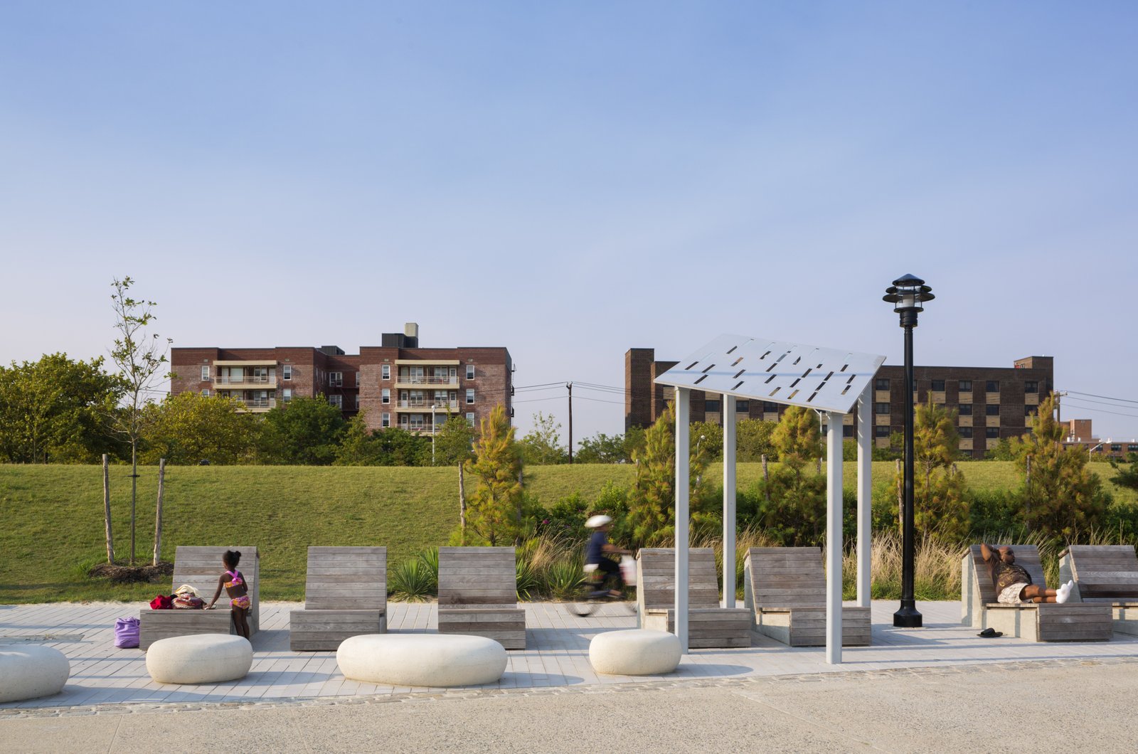 A park seating area with wooden lounge chairs, stone accents, and a metal shade structure.