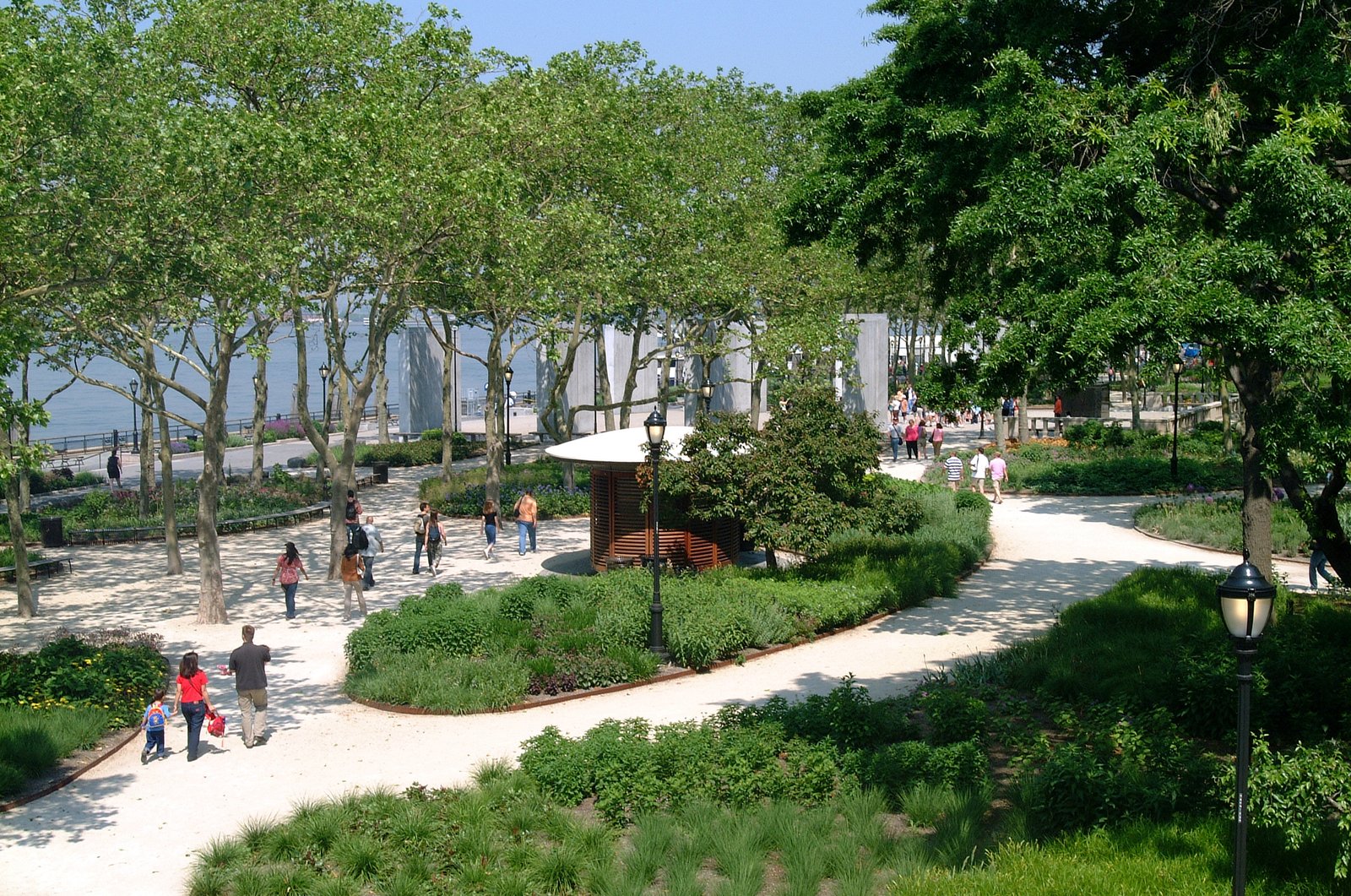 Pathways lined with dense foliage and trees lead to a waterfront in a vibrant urban park.