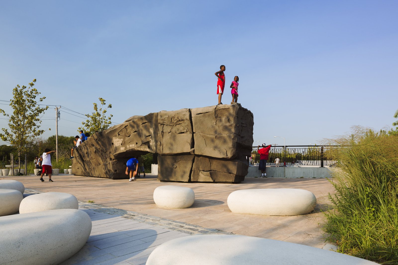 Children climb and play on a large sculptural rock structure surrounded by stone seating.