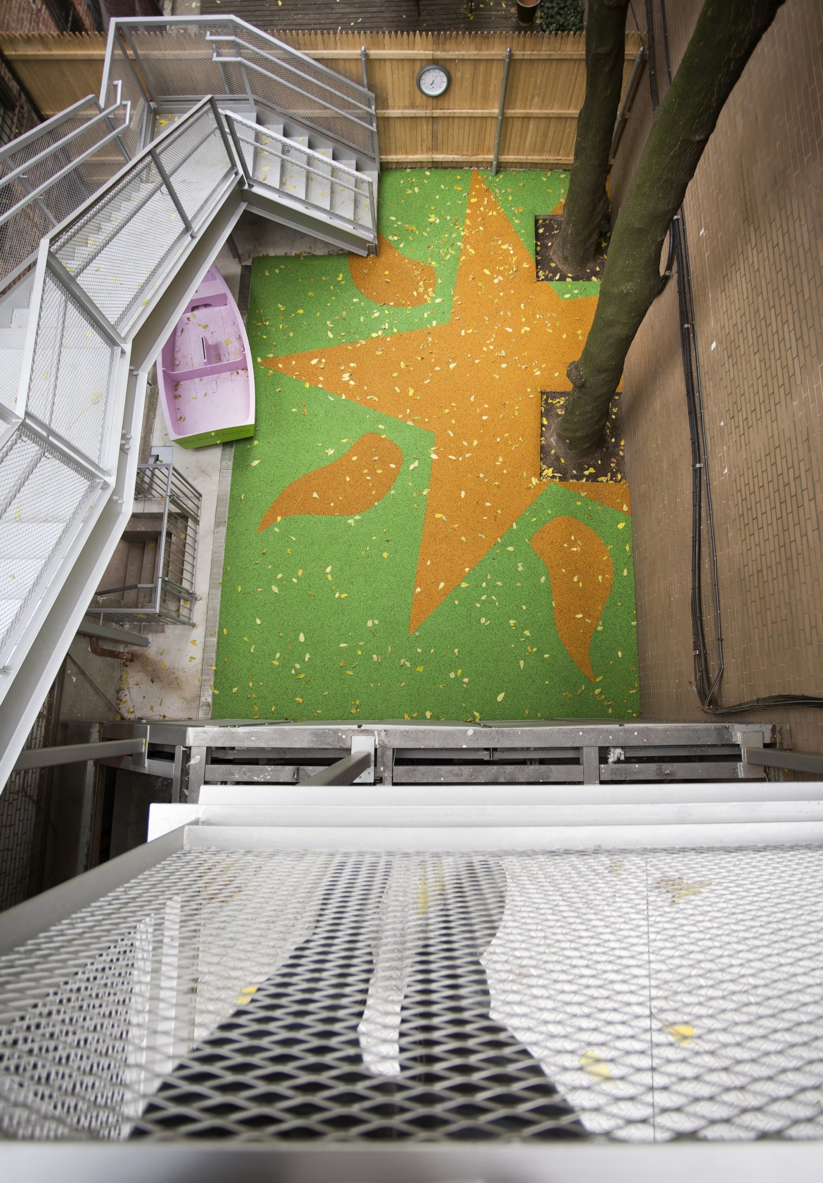 An aerial view of a colorful outdoor play area with trees, a staircase, and a patterned rubber surface.