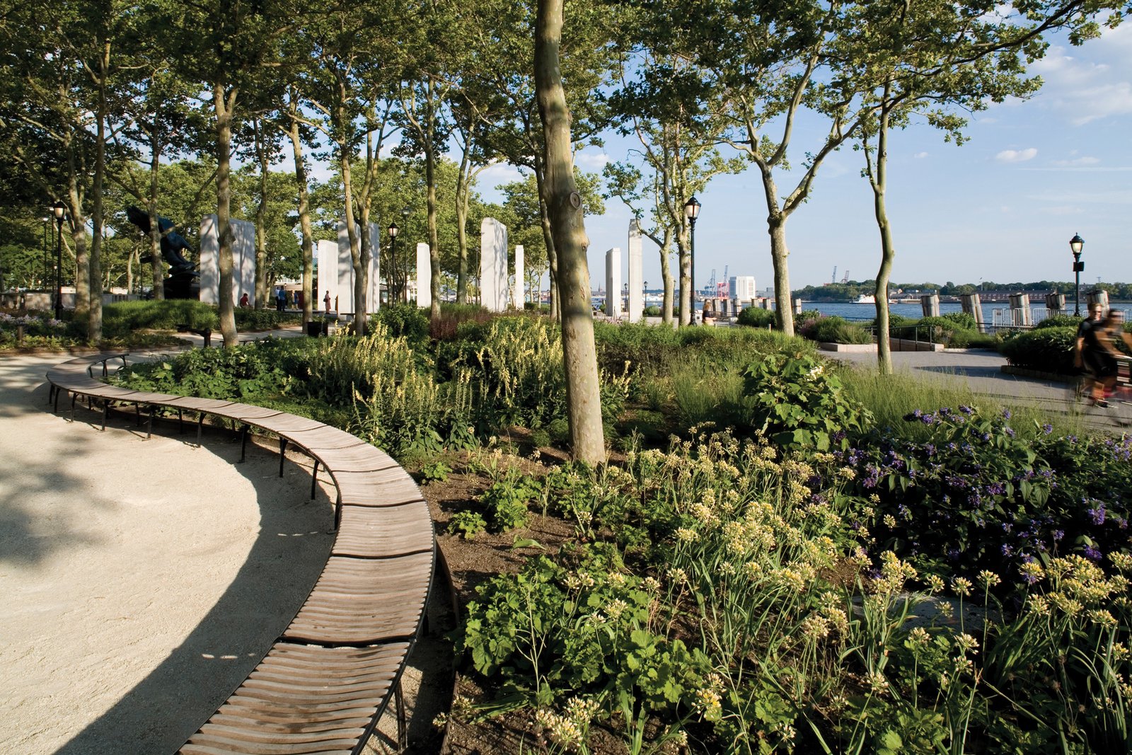 Curved wooden benches sit near lush gardens with views of the New York Harbor in the distance.