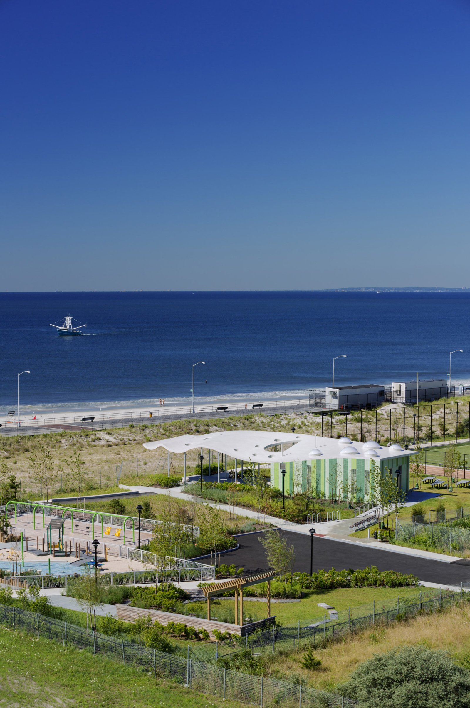 An aerial view of PlaNYC Far Rockaway Park with a pavilion, playground, and dunes by the Atlantic Ocean.