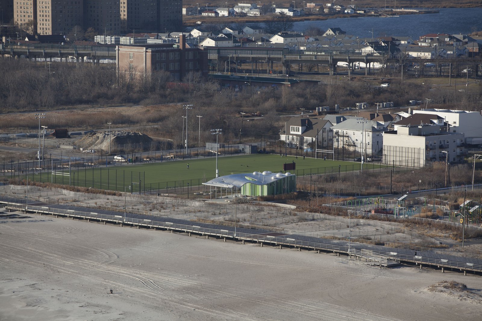 Aerial view of Far Rockaway Park showing a green field, comfort station, boardwalk, and surrounding buildings.